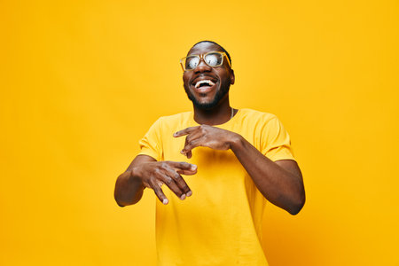 Happy young man wearing yellow shirt and sunglasses, joyful expression, isolated on bright yellow background, cheerful mood, stylish and modern look, ideal for vibrant lifestyle imageryの写真素材
