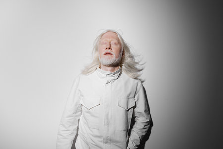 Portrait of a serene elderly man with long white hair and a beard, dressed in a white outfit against a neutral background, conveying a sense of peace and tranquilityの写真素材