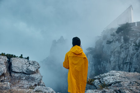 A solitary figure in a vibrant yellow raincoat, standing atop a misty mountain peak a journey through nature and solitudeの写真素材
