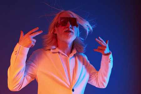 Stylish man with long white hair and oversized sunglasses, striking a confident pose against a vibrant blue and purple background, showcasing modern fashion and charismaの写真素材