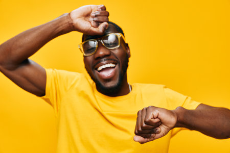 Happy man dancing joyfully in yellow outfit and sunglasses, expressing fun and energy against a bright yellow background, ideal for cheerful lifestyle concepts and vibrant imageryの写真素材