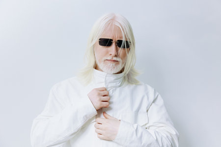 Stylish elderly man with long white hair and sunglasses in a white outfit, looking confidently at the camera against a light gray background Contemporary fashion and modern aestheticsの写真素材