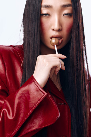 Woman with black hair and red leather jacket enjoying a lollipop in urban settingの写真素材