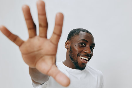 Smiling young man with a playful gesture, wearing a plain white t shirt against a neutral background His joy and confidence radiate through his expression, making it a captivating portraitの写真素材