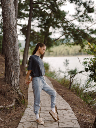 Young woman in casual outfit standing on a pathway along a river, enjoying the natural surroundings Peaceful outdoor lifestyle conceptの写真素材