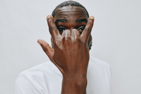 Black man making a hand gesture symbolizing love and appreciation, dressed in a white t shirt,...