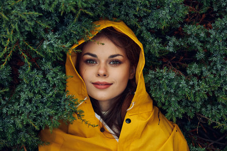 Woman in Yellow Raincoat Surrounded by Green Trees and Bushes in a Beautiful Forest Settingの写真素材