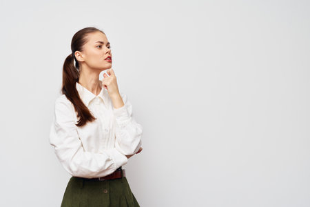 thoughtful woman in white shirt, pondering expression, standing against simple gray background, arms crossed, confidence, youthful appearance, modern style, professional look, engagementの写真素材