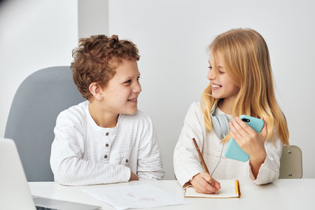 Smiling Siblings Playing Selfie Two happy children, a boy and a girl, are sitting indoors in a cozy home interior They are using a smartphone to take a selfie together, capturing their joyful momentsの写真素材