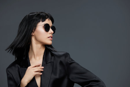 Asian woman wearing a black suit and sunglasses, posing confidently against a gray backgroundの写真素材