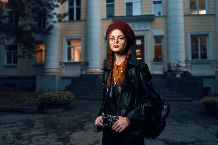 Stylish woman in leather jacket and glasses stands confidently in front of historic buildingの写真素材