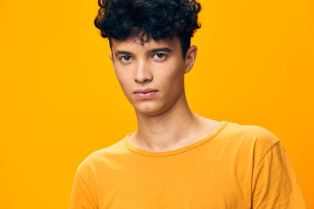 Portrait of a young man with curly hair wearing a bright yellow shirt against a vivid yellow background, showcasing a confident expression and modern styleの写真素材
