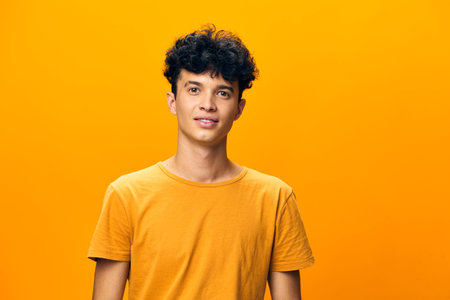 Young man in a bright yellow shirt smiling against an orange background, showcasing confidence and positivity in contemporary fashion photography Emphasizing youthfulness and vibrancyの写真素材