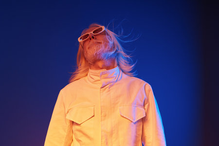 Stylish man with long hair in sunglasses against a vibrant blue and orange background, showcasing a...