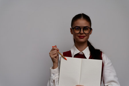 Young woman with glasses holding an empty notebook and a pencil against a plain white background, exuding confidence and a positive attitude while ready to share ideasの写真素材