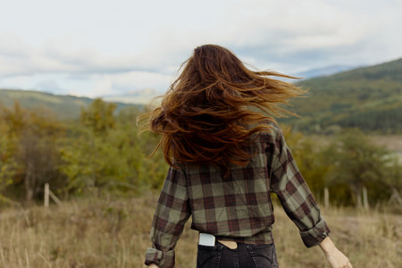 A woman explores the beauty of nature as her hair dances in the wind across a serene grassy fieldの写真素材