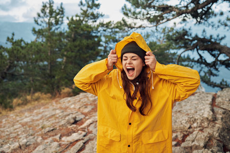 A woman in a yellow raincoat standing triumphantly on a mountain peak, embracing the beauty of nature and adventureの写真素材