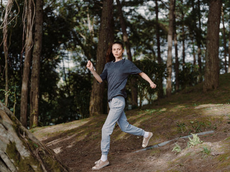Young woman running joyfully through a forest, wearing casual clothes and sneakers, surrounded by...