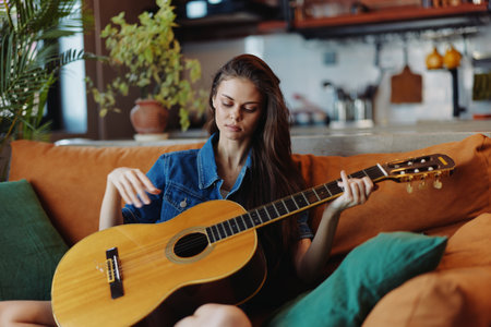 Young woman playing acoustic guitar on sofa in front of coffee table in cozy living room settingの写真素材