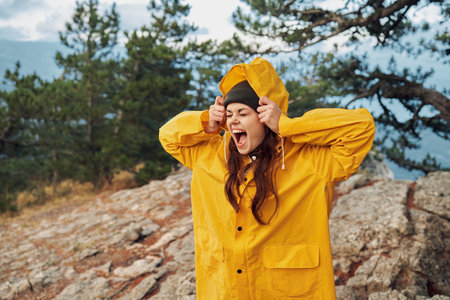 Woman in yellow raincoat admiring breathtaking mountain view with hands on head in awe of travel beautyの写真素材