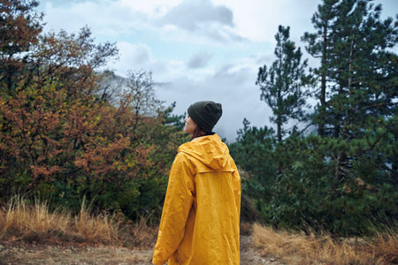 Solo traveler in a vibrant raincoat standing contemplatively on a dusty country road, gaze fixed on...