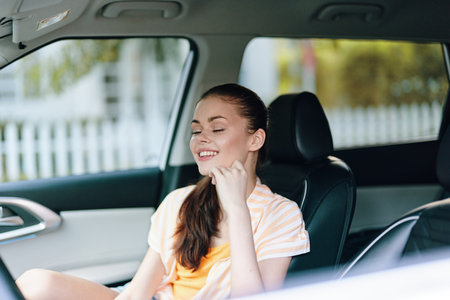 Happy young woman smiling in a car seat with a relaxed expression, wearing a casual orange and white outfit, enjoying a sunny day outdoors Her long hair is downの写真素材