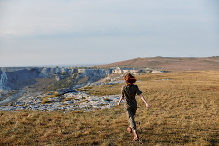 Woman walking through a grassy field with a mountain in the background in travel and nature settingの写真素材