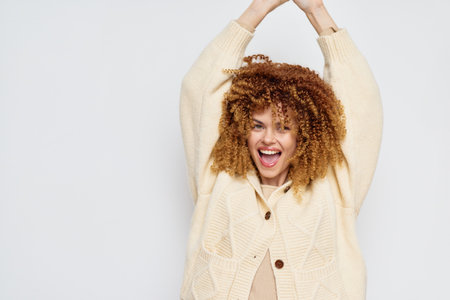 Happy woman celebrating with raised arms, wearing a cozy knitted cardigan, against a minimalistic light background Expression of joy and positivity in casual attireの写真素材