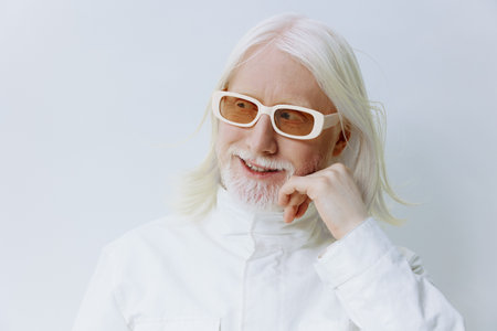 smiling elderly man with long white hair wearing white sunglasses and a white outfit against a light background, thoughtful expression, modern and stylish vibeの写真素材