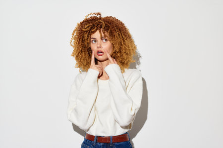 surprised woman with curly hair, wearing a white sweater, against a plain white background showing confusion or astonishment with expressive facial gesturesの写真素材