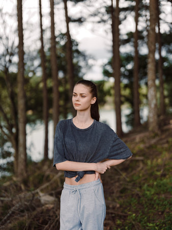 Thoughtful young woman standing in a serene forest, wearing loose fitting casual clothes, reflecting on nature and personal emotions Peaceful outdoor ambianceの写真素材