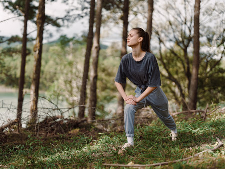 Young woman in gray sportswear stretching in a tranquil forest, practicing mindfulness and fitness in nature Wellness and active lifestyle conceptの写真素材