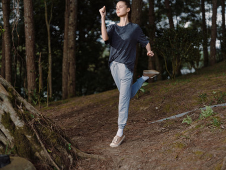 Energetic young woman jogging in a wooded area, wearing casual athletic clothing, expressing joy and determination Healthy lifestyle and nature exploration conceptの写真素材