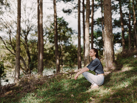 Calm young woman practicing yoga outdoors in a serene forest, surrounded by trees and nature Wellness and relaxation conceptの写真素材