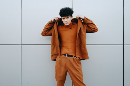 Stylish young man adjusting his brown jacket against a gray background