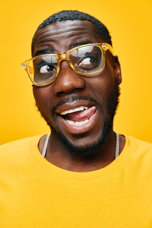 Portrait of a cheerful young man in yellow glasses and a bright yellow T shirt against a vibrant yellow background, showcasing joy and confidenceの写真素材