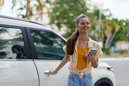 Young woman with a smartphone near a modern car, vibrant city background, wearing a casual outfit with a smile, exuding confidence and joy in daily lifeの写真素材