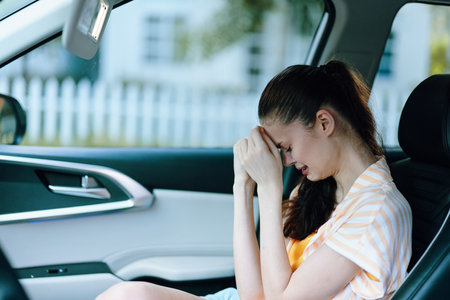 Sad young woman sitting in a car, holding her head in distress Light colors and blurred background...