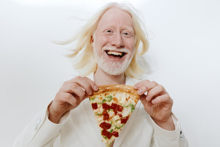 Happy man enjoying pizza slice, bright background, joyful expression, light hair and beard, casual attire, conveying fun and satisfaction from foodの写真素材