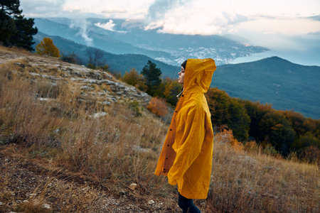 A solitary figure in a vibrant yellow raincoat standing atop a hill, gazing over a serene valley Nature, exploration, solitude and contemplationの写真素材