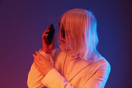 Modern businessperson with long white hair talking on a smartphone, set against a colorful gradient background of blue and purple tones, representing contemporary communicationの写真素材
