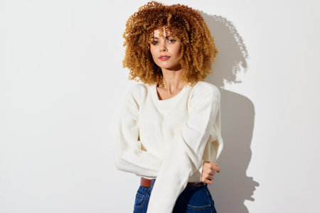 Model with curly hair in a white sweater posing against a plain white background Soft lighting...