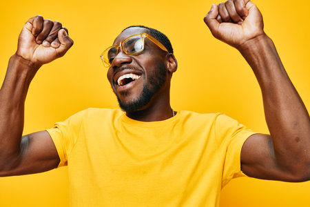 Happy man celebrating with joy, wearing yellow shirt and glasses, vibrant expression against a bright yellow background Energetic and uplifting mood, perfect for lifestyle themesの写真素材