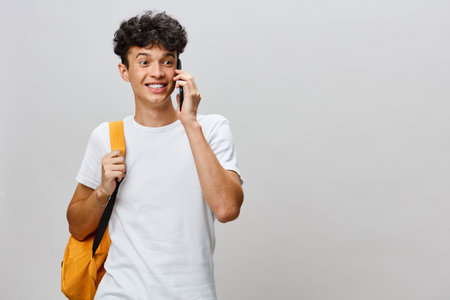 Young man talking on the phone, smiling, wearing a casual white t shirt and holding a yellow...