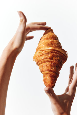 Person holding a croissant in one hand over a white backgroundの写真素材