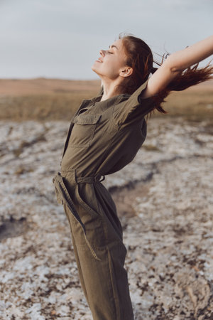Woman in olive green jumpsuit standing with outstretched arms in desert landscape for travel and fashion conceptの写真素材
