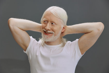Happy elderly man smiling with white hair, dressed in a plain white t shirt, set against a neutral...