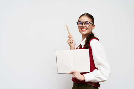 Smiling student holding a blank notebook with a pen, wearing glasses and a red sweater, on a plain white background, showcasing creativity and enthusiasm for learningの写真素材