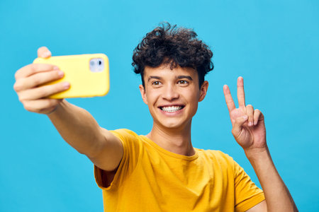 cheerful young man taking a selfie on a bright blue background, dressed in a yellow t shirt,...