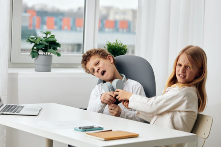 Happy children studying and playing online together at home A boy and a girl, sitting at a table in...